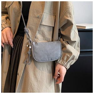 Détail de sac besace gris mat montrant les coutures fines et le logo embossé