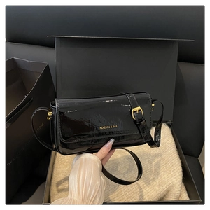 Close-up of black patent leather shoulder bag with golden brand logo and buckle detail