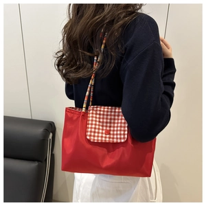 Detail of red canvas tote with red-white plaid flap and colorful braided shoulder straps