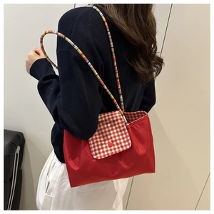 Detail of red nylon tote bag featuring red and white checkered flap and striped handle