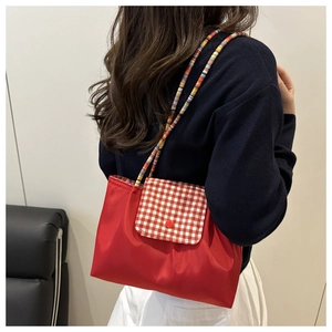 Detail of red nylon tote bag featuring plaid flap and colorful braided shoulder strap