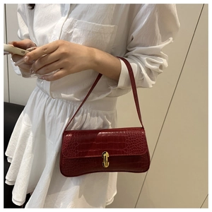 Detail of burgundy crocodile pattern shoulder bag with golden buckle on a white dress