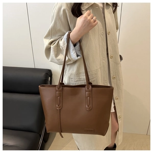Dettaglio della borsa tote in pelle marrone con etichetta su modella con cappotto beige