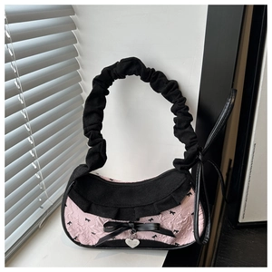 Detail of pink and black fabric bag featuring a silver heart pendant and bow