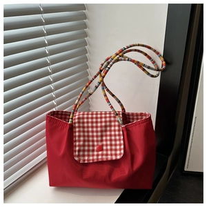 Detail of red nylon tote bag with plaid flap and colorful braided rope handle
