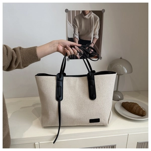Dettaglio della borsa tote in tela bianco sporco con manici in pelle nera sul tavolo