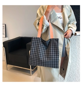 Détail d'un sac cabas en toile à carreaux avec poignées orange porté par un mannequin