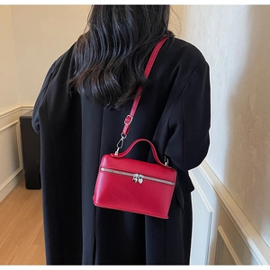Detail of red leather crossbody bag with heart-shaped silver zippers on black coat