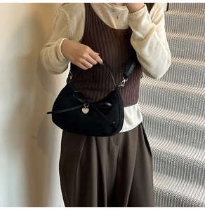 Detail of black suede dumpling bag with a bow knot and heart pendant shown on model