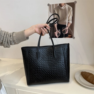 Elegant black woven leather tote bag for women shown in a minimalist interior setting