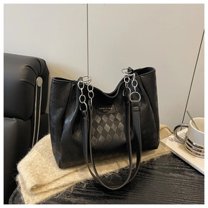 Detail of black leather tote bag with diamond quilted texture and gold chain straps