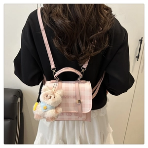 Pink checkered small backpack with plush bear charm worn on a model back in a chic studio