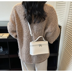 Close-up of a white lychee grain leather crossbody bag held by a model in a cozy setting