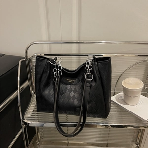 Chic black quilted tote bag with silver chain strap on a minimalist display stand