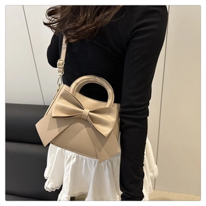 Detail of minimalist beige handbag featuring a large bow and detachable shoulder strap