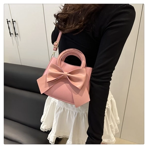 Close-up of pink bow handbag with circular handle and adjustable shoulder strap worn by model