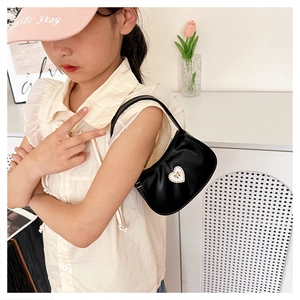 Chic black heart-shaped hobo bag with pearl bow detail worn by a model in casual style