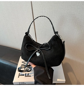 Detail van zwarte suède handtas met lederen strik en een zilveren hartvormige hanger