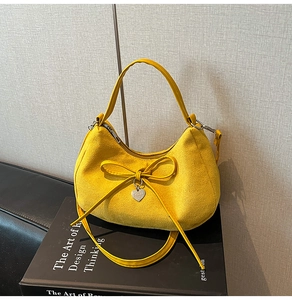 Macro detail of yellow suede dumpling bag with decorative bow and heart pendant