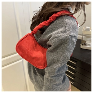 Détail d'un sac sous les aisselles en daim rouge avec bandoulière plissée sur modèle