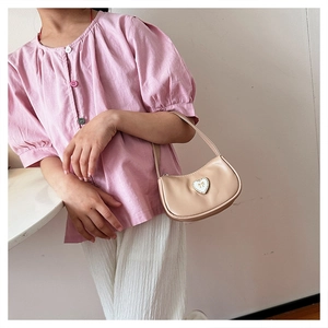 Close-up of beige crescent hobo bag featuring a white heart charm and golden bow detail
