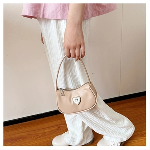 Detail einer cremigen beige Minibandtasche mit weißem Herzanhänger und Schleife
