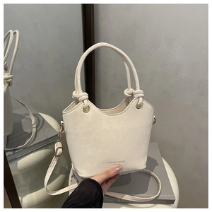 Detail of cream bucket bag with unique knot handle and metallic strap on a reflective surface
