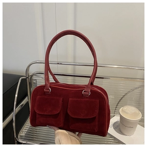 Détail du sac à bandoulière en suède bordeaux avec deux poches avant sur une chaise