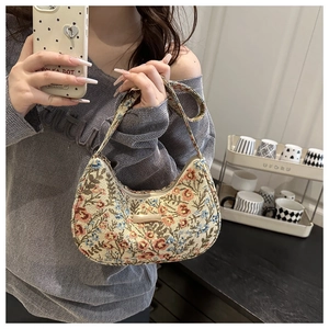 Close-up of vintage floral jacquard fabric and metal logo plaque on a crescent hobo bag