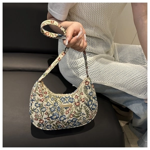 Detailed close-up of floral jacquard fabric and gold logo plaque on a retro hobo bag