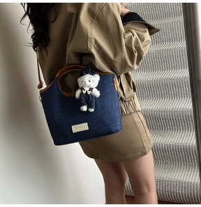 Chic denim bucket bag with brown leather trim and cute plush bear charm on model