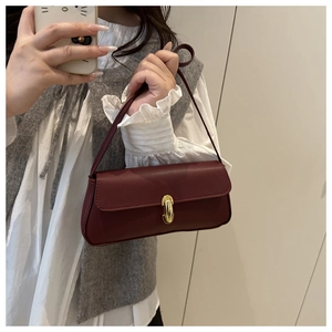 Detail of burgundy leather shoulder bag with gold metal clasp on a textured strap