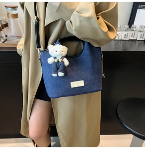 Detail of blue denim tote bag with leather logo patch and cute plush bear charm