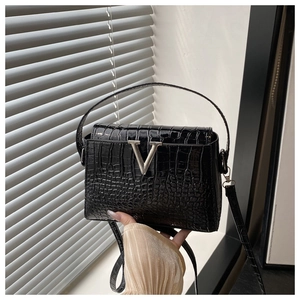 Close-up of black crocodile pattern leather with metallic V-buckle on a crossbody bag