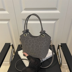 Gray leopard bucket bag with gold hardware and knotted top handles on a book