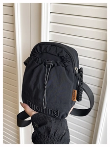 Detailed macro view of black nylon crossbody bag featuring orange fashion label and drawstring