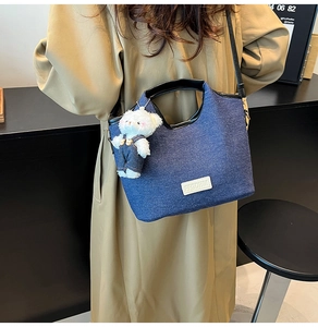 Detail of blue denim shoulder bag with leather handle and white teddy bear charm on model