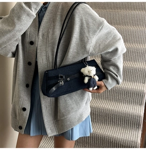 Detail of dark blue denim baguette bag with PU leather straps and a cute teddy pendant