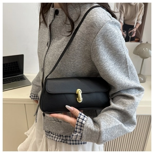 Close-up of black leather shoulder bag with gold metal buckle on a minimalist desk