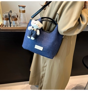 Detail of blue denim shoulder bag with leather patch and cute teddy bear charm