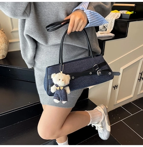 Detail of blue denim shoulder bag with leather crisscross straps and cute plush bear charm