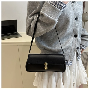 Detail of a black leather baguette bag with a golden turn-lock clasp on shoulder