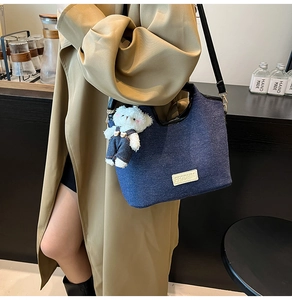 Detail of blue denim shoulder bag featuring a cute plush bear charm and leather strap