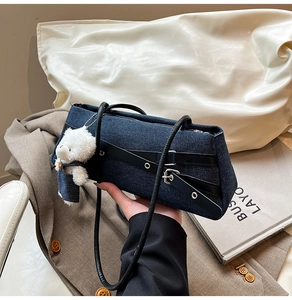 Detail of blue denim shoulder bag with leather straps and a cute white bear pendant