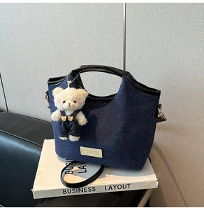Detail of dark blue denim shoulder bag with leather trim and white plush bear charm