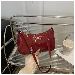 Detalle de bolso de hombro en charol burdeos con hebilla de lazo metálico dorado