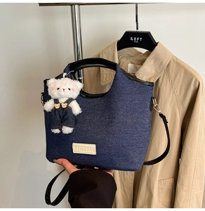 Detailed view of dark blue denim bag with black trim and a cute plush bear charm