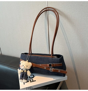 Detail of denim underarm bag with leather straps and a cute plush bear charm