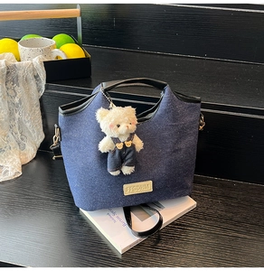 Detail der blauen Denim-Tasche mit Lederbesatz und Plüschbär-Anhänger auf Holzstufen