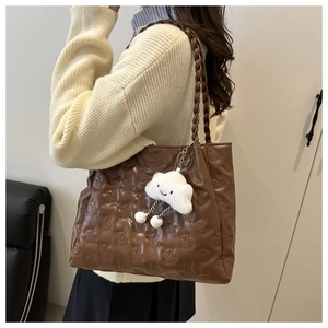 Detail of brown tote bag featuring bear embossed pattern and white plush charm accessory